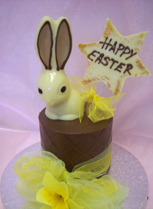 a picture of one white chocolate bunny rabbit on a milk chocolate tier.  Decorated with yellow flowers and mounted on a silver display disc.