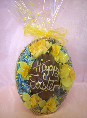 a picture of a Milk chocolate Easter egg nesting in a decorative basket, decorated with white chocolate and yellow flowers.
