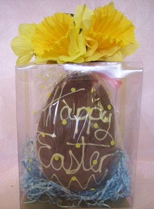 a picture of a Milk chocolate Easter egg nesting in a transparent box, decorated with white chocolate and yellow flowers.