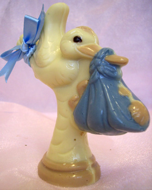 a picture of a white chocolate stork carring a baby decorated with milk, dark and coloured chocolate