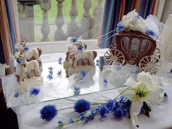a picture of a milk chocolate wedding carriage, with white chocolate horses, decorated ribbon and blue flowers