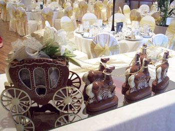 a picture of a milk chocolate wedding carriage and horses, decorated with ribbon, flowers and a gold rein