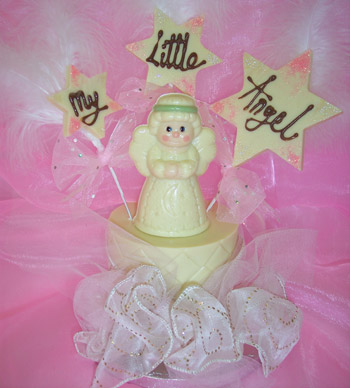 a picture of a white chocolate angel on a tier, decorated with coloured chocolate. Large chocolate snowflakes message reads 'My Little Angel'