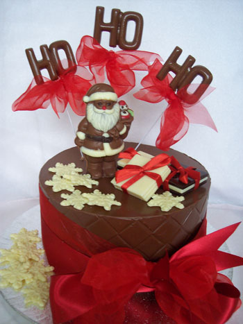 a picture of a milk chocolate Father Christmas on a chocolate tier, decorated with coloured chocolate and red ribbon.  Chocolate letters reads 'Ho Ho Ho'