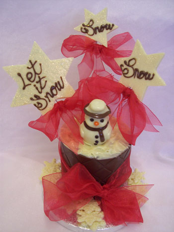 a picture of a white chocolate snowman decorated with coloured chocolate and red ribbon on a chocolate tier.  Large chocolate snowflakes reads 'Let it Snow'